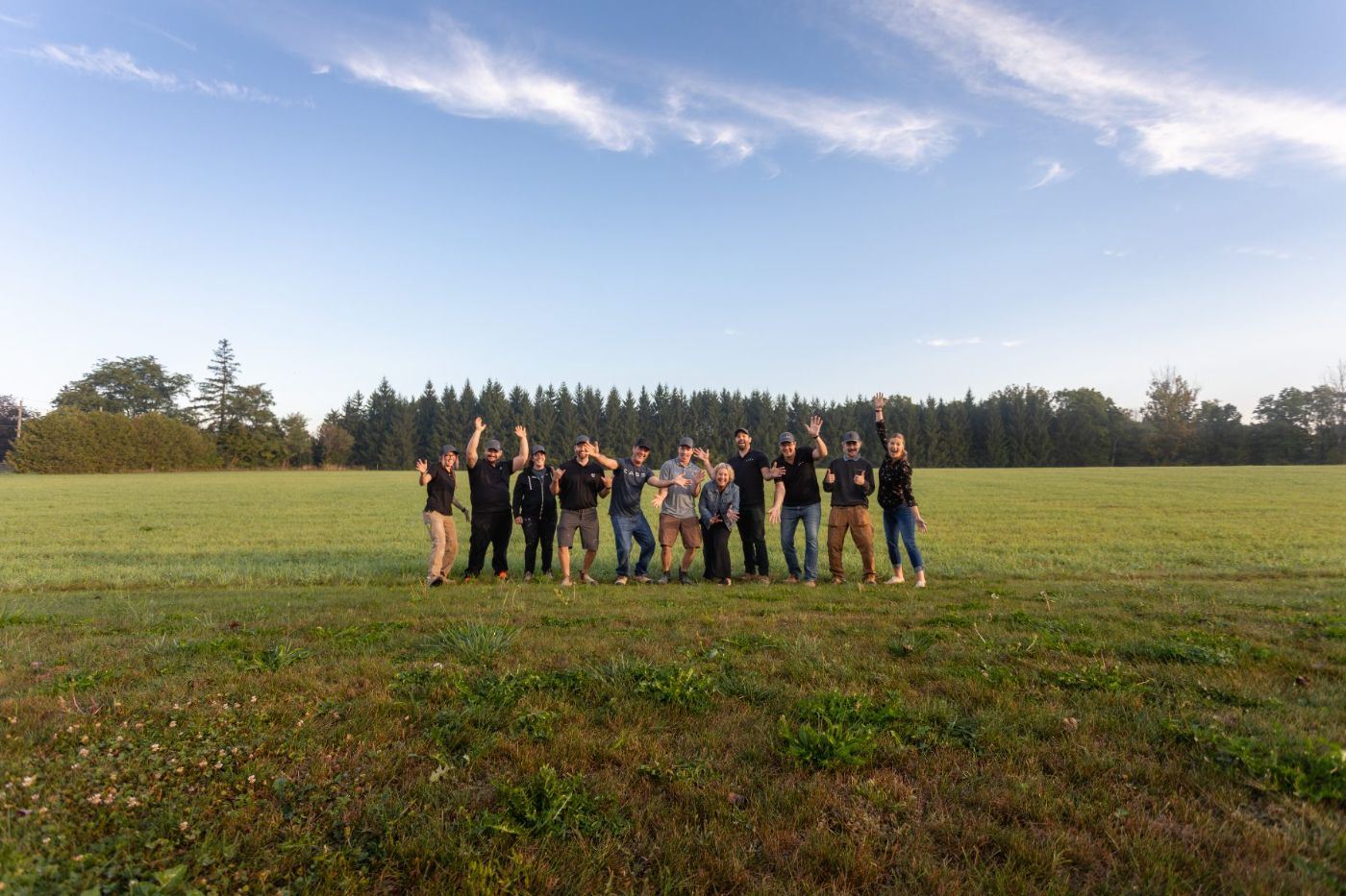 The Cass Construction team standing together in an open field, waving, with a pine treeline behind them