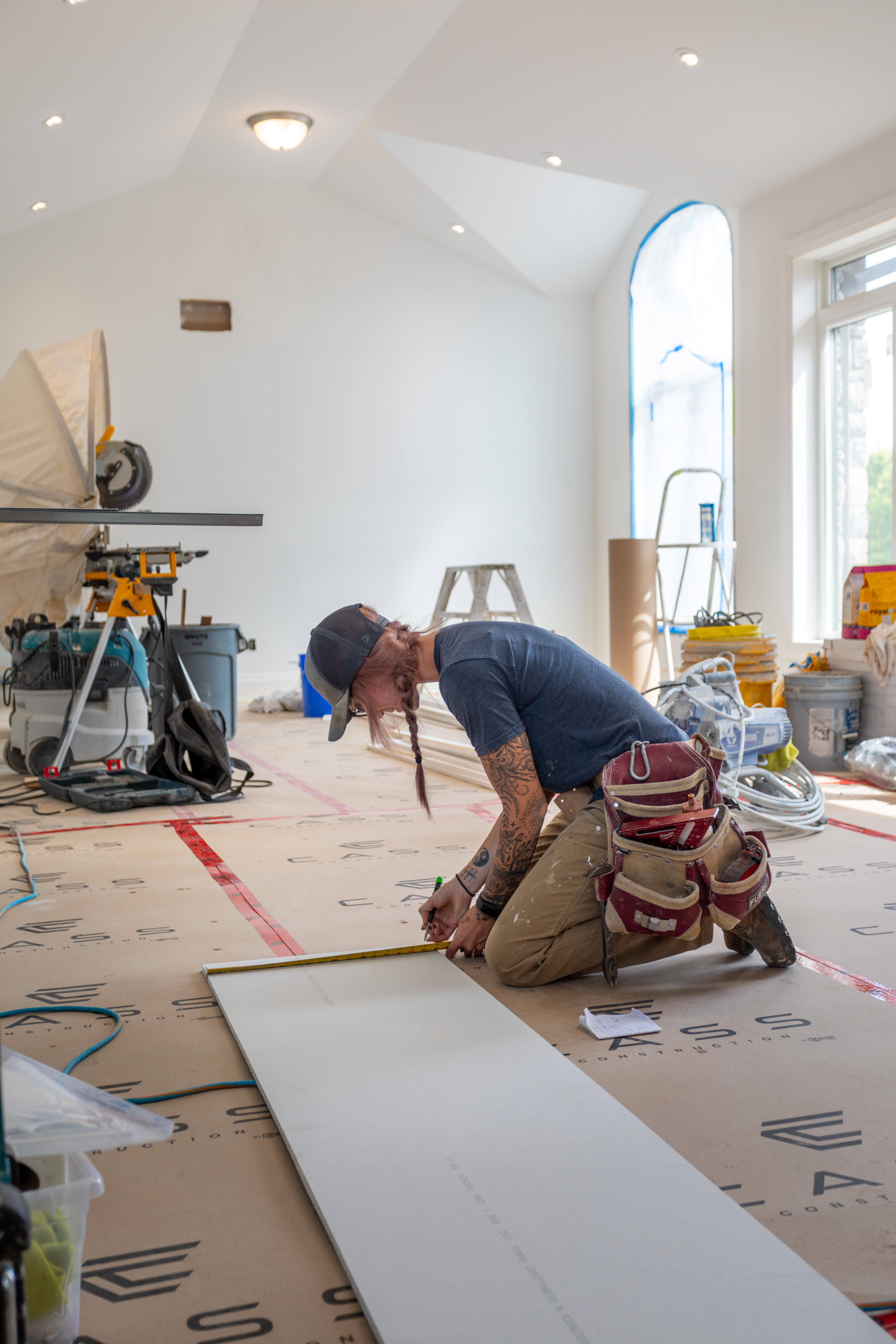 A Cass carpenter measuring and marking drywall on a protected floor during an interior build