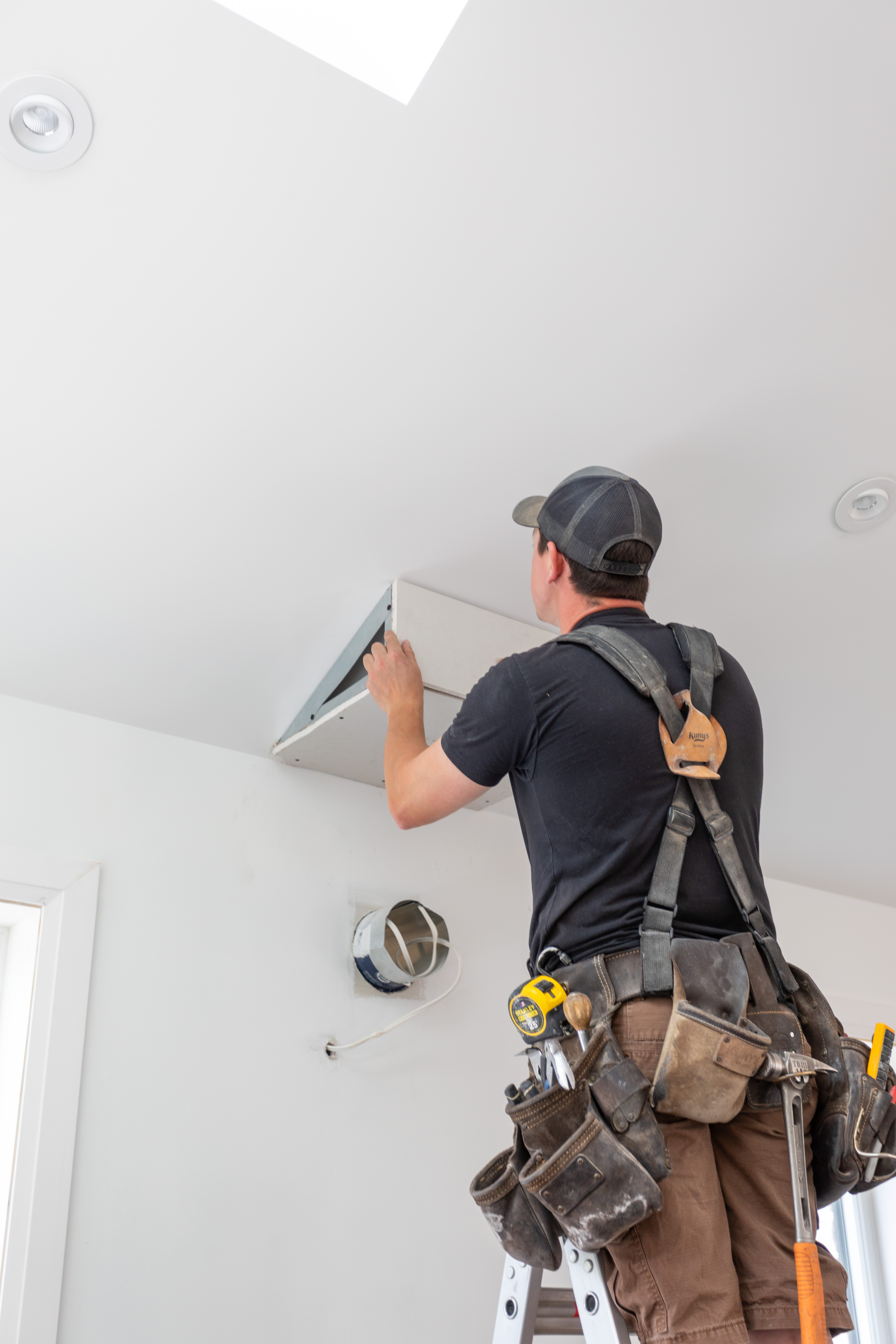 A Cass carpenter on a ladder fitting a skylight shaft into a finished ceiling