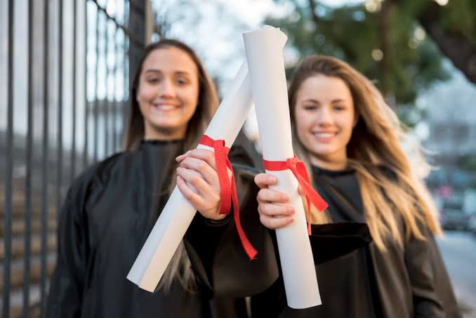 Two graduates holding diplomas